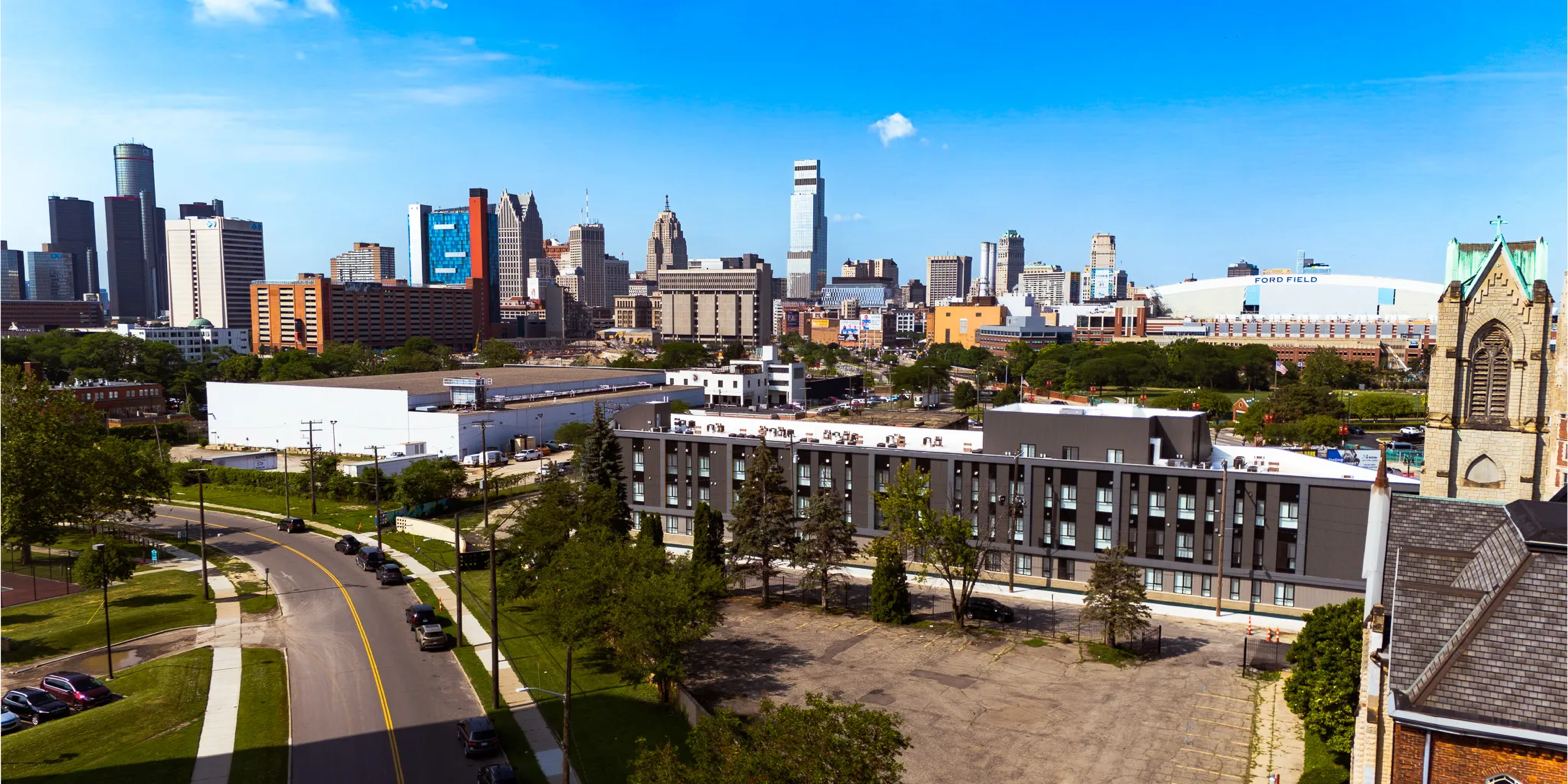 The Hive on Russell, a four-story charcoal building in Detroit, with the downtown skyline and Ford Field beyond