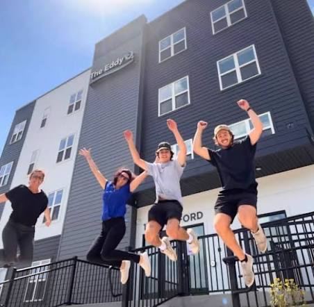Four people jumping in celebration in front of The Eddy in Eau Claire